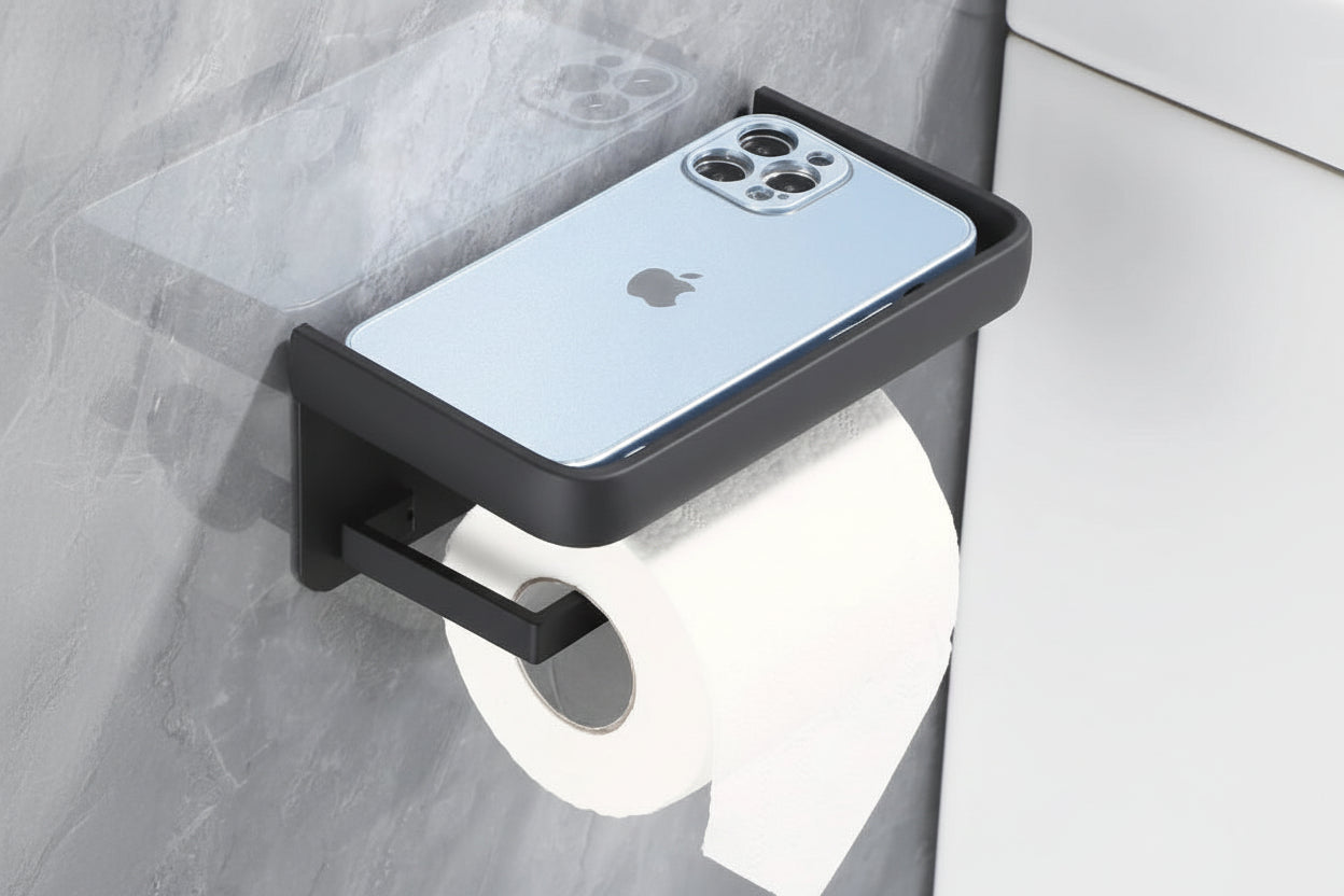 Black roll paper holder with shelf holding a phone, mounted on a wall.